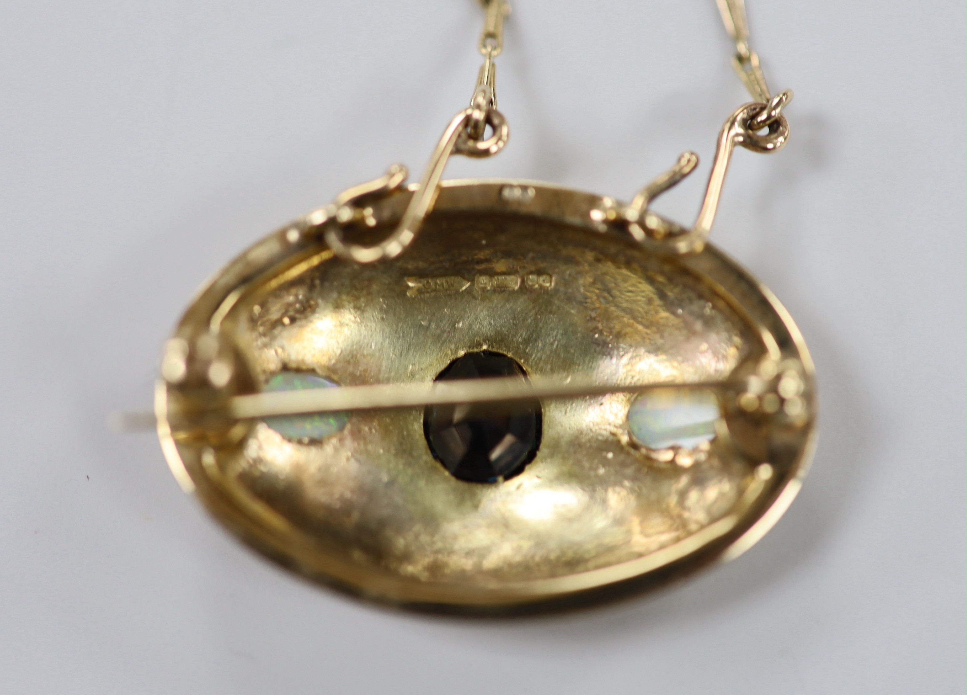 A 1970's 9ct gold and gypsy set single stone sapphire and two stone white opal set oval pendant brooch, 34mm, on a 9ct gold chain, 46cm, gross weight 15.9 grams.